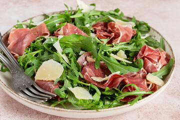 Fresh arugula salad with prosciutto and grated parmesan cheese, on a plate, homemade, no people,