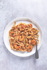 Fettuccine pasta with shrimp, spicy in soy sauce, on a grey plate with a fork, close-up,
