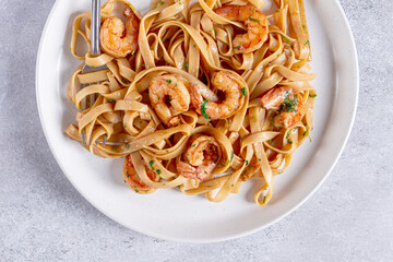 Fettuccine pasta with shrimp, spicy in soy sauce, on a grey plate with a fork, close-up,