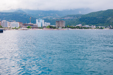 Fototapeta premium Coastal town skyline viewed from sea on cloudy summer day. Waterfront architecture, beach tourism and seaside development in Montenegro.