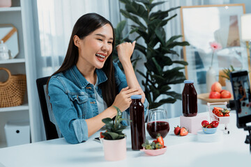 Smiling young beautiful Asian reviewing tasty mixed strawberry and cherry juice detox drinks, showing healthy product to promote for special promotion selling on social media online record. Stratagem.