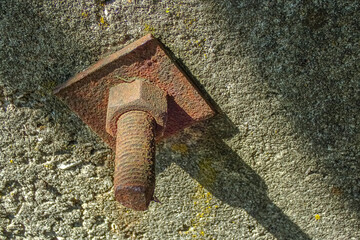Closeup of rusty metal bolt in concrete wall. Corroded industrial texture and detail of aged...