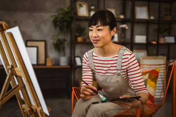 one woman female artist paint canvas on easel hold paintbrush at home