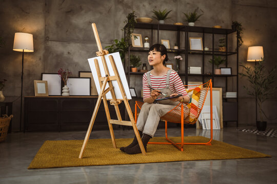 one woman female artist paint canvas on easel hold paintbrush at home