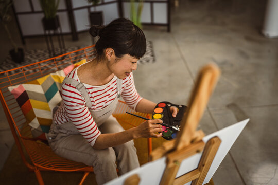 one woman female artist paint canvas on easel hold paintbrush at home