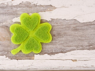 A green shamrock with four hearts on it is on a wooden surface