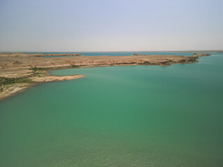 Aerial view, the drone moves above the turquoise Kuimazar Reservoir. The barren shoreline stretches...