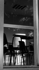 Black and white photo of an empty classroom viewed through a window. Symbolic image of silence, memory, or abandonment in educational spaces.