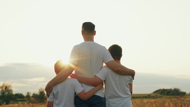 Son hugs father with arms on outdoors. Kid son hugs dad on sunny meadow. Father loves his son, happy hugs of child dad. Family walk in nature. Family, dad son walk together in sun park. Kid boy parent