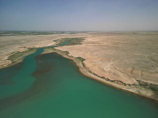 Aerial view of winding river as it joins Kuimazar Reservoir. The river curves through dry steppes. Sparse green vegetation lines the banks. The water is clear, creating a beautiful contrast