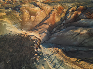 Aerial view sweeps above mineral-stained ridges and dramatic desert ravines. Erosion carves beauty...