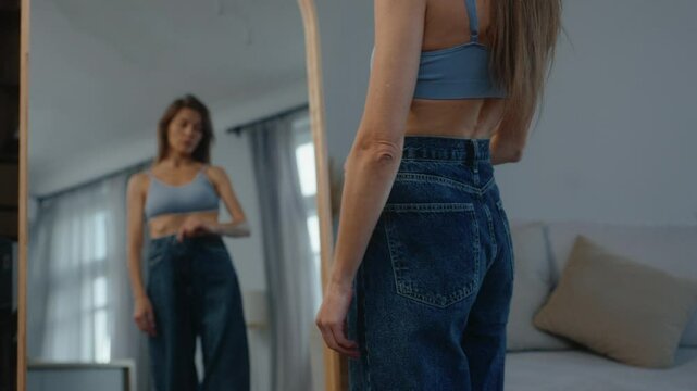 Anorexic slim body woman wearing big jeans standing front of mirror