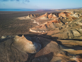 The camera glides above crescent-shaped hills of Aktumsik Cape at sunrise. Sharp shadows and ochre tones highlight the area's arid beauty and ancient past