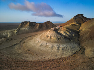 Sunrise casts long shadows on Aktumsuk's prominent peaks by the Aral Sea. The camera reveals rolling hills, deep valleys, and shifting morning clouds overhead