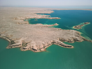 Aerial view of Kuimazar Reservoir in Uzbekistan with turquoise water meeting arid desert. Contrasts of land and lake create a unique, tranquil landscape for exploration and travel