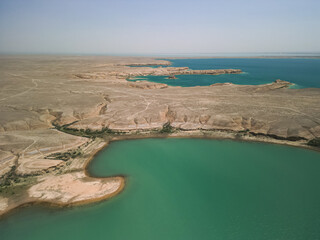 Peninsula juts into turquoise Kuimazar Reservoir, surrounded by desert land. Bright water contrasts sharply with the arid Central Asian environment of Uzbekistan.
