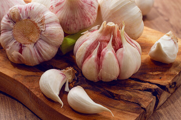 Close-up of several heads and cloves of fresh garlic lying on a wooden chopping board, natural...