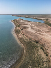 Sandy shoreline meets vivid blue water at Kuimazar Reservoir in Uzbekistan. Dry terrain and curved lines emphasize the contrast of water and desert environments in Central Asia