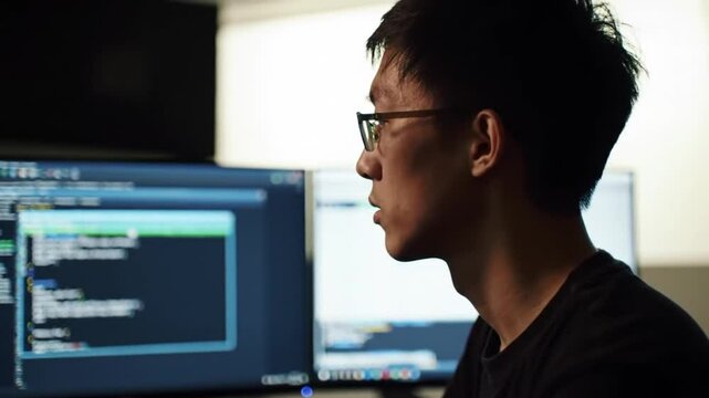 Focused cybersecurity specialist analyzing code on multiple monitors in workspace