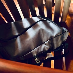 photograph of a high quality wooden chair, in which there is a laptop backpack with a cat inside, with only one eye and one ear visible.