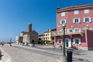 A picturesque sunlit scene captures a segment of the charming Piran coastline in Slovenia,...