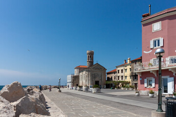 A picturesque sunlit scene captures a segment of the charming Piran coastline in Slovenia,...