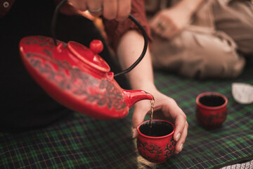 tea ceremony and tea drinking in nature. red teapot and red cups. green chinese tea is poured into a cup from a teapot. picnic with tea ceremony.