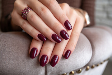 Elegant deep burgundy manicure with detailed ring showcased on soft fabric backdrop