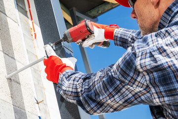 Construction Worker Using a Drill to Secure Metal Framing in Bright Daylight Outdoors