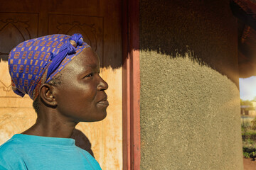 village single african woman with headscarf sited in front of the house , in the yard, close...