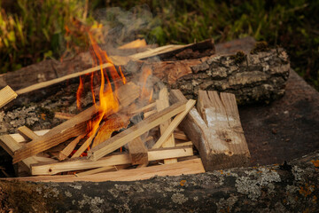 Bright orange flames rise from burning firewood arranged on a stone surface in an outdoor setting,...