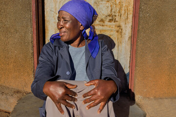 village single old african woman with headscarf sited in front of the house , in the yard, close portrait