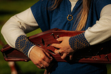 Close-up of hands playing a traditional wooden string instrument, worn with a blue folk costume...