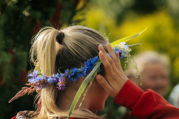 Woman in traditional clothing wearing a white headscarf and a vibrant wildflower crown, captured in...