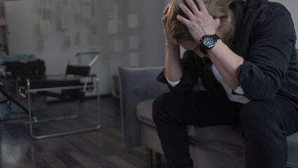 A man in deep depression and apathy, sitting on the couch with his head in his hands