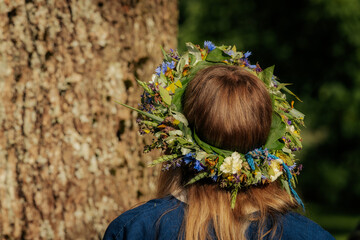 Close-up of a flower crown made of colorful wildflowers and greenery on a woman's brown hair,...