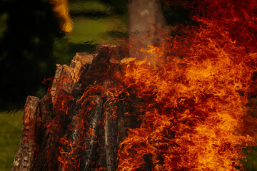 Tall bonfire burning intensely with orange flames reaching high, surrounded by rocks and trees...