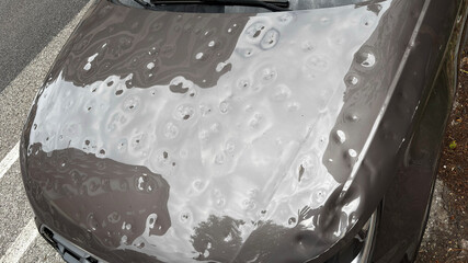 Car hood severely damaged by hail, showing multiple dents and surface imperfections caused by the...