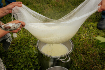 Fresh cheese is being strained through cloth, held by people outdoors using large green leaves,...