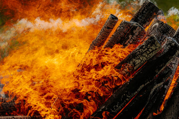 Intense orange flames engulf burning firewood in a large bonfire, with vivid textures of charred...