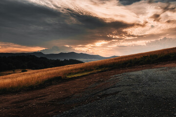 Sunset over rippling hills, with dramatic clouds and golden grasses, creating a picturesque mountain landscape in warm colors