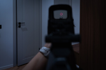 Home defense concept: first-person view of a woman holding an assault rifle and aiming at a door...