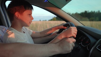 Dad teaches his little son to turn steering wheel while sitting in driver seat of auto. Father travels with children by car. Driver dad child son driving car. Happy family, childhood. Driving car kid