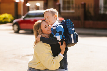 Mother hugging son with backpack on first day of school, happy family moment, back to school outdoors