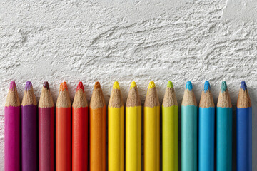 A row of colored pencils arranged in a rainbow spectrum against a textured white background surface