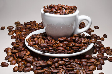 Coffee beans with a small coffee cup and saucer isolated against a white background