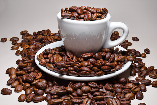 Coffee beans with a small coffee cup and saucer isolated against a white background
