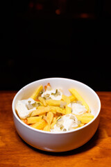 French fries in a white bowl topped with creamy white sauce and chopped pickles. A delicious and simple snack or side dish served on a wooden table