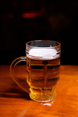 Pint of light beer in a glass mug on a wooden bar counter. Warm lighting and dark background create a cozy pub atmosphere