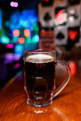 Dark beer in a classic 0.5L glass mug on a wooden bar counter. Colorful blurred lights in the background create a cozy pub or nightclub vibe